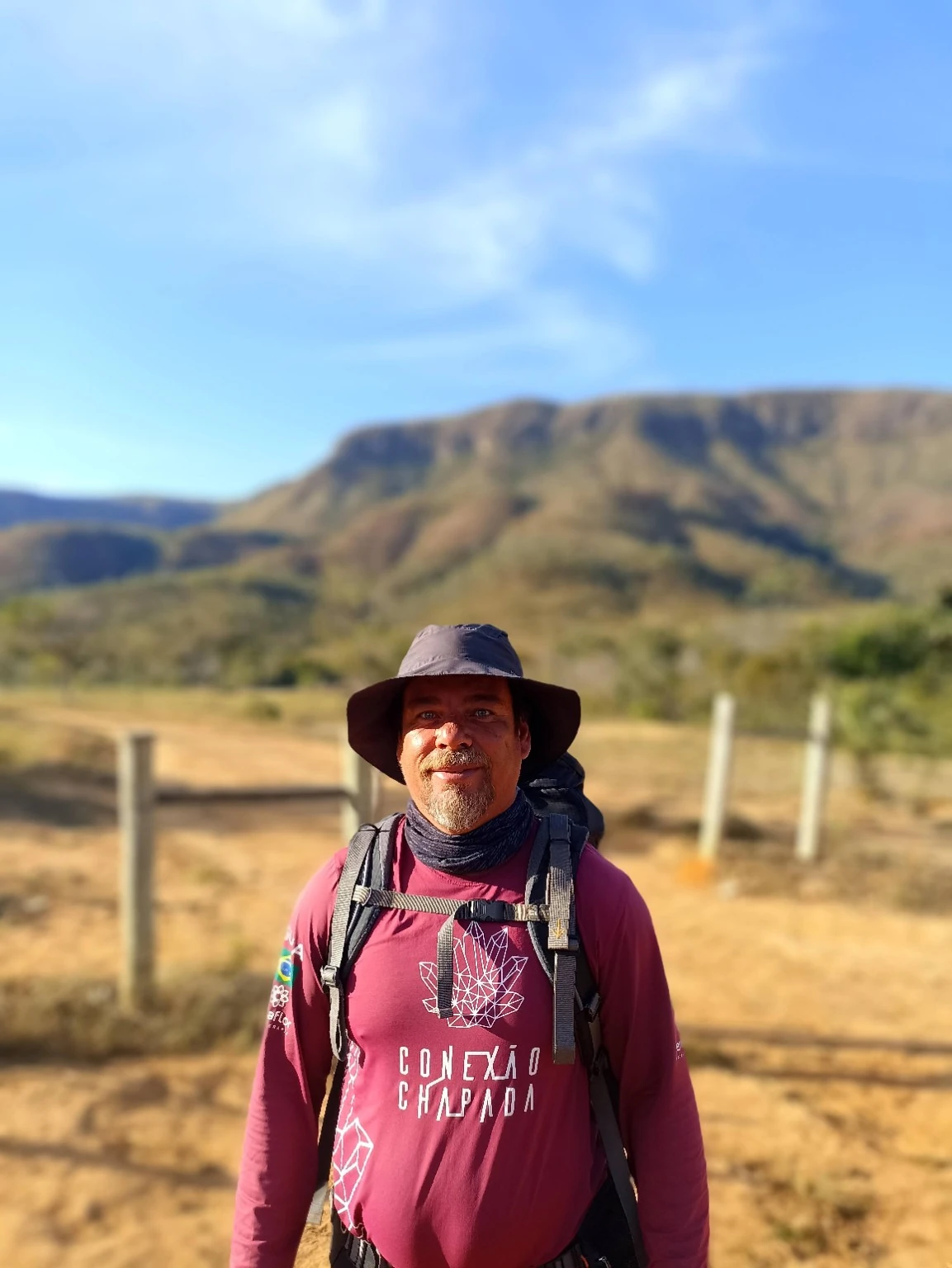 Fabiano Selva, com chapéu e mochila, diante de uma paisagem de serra